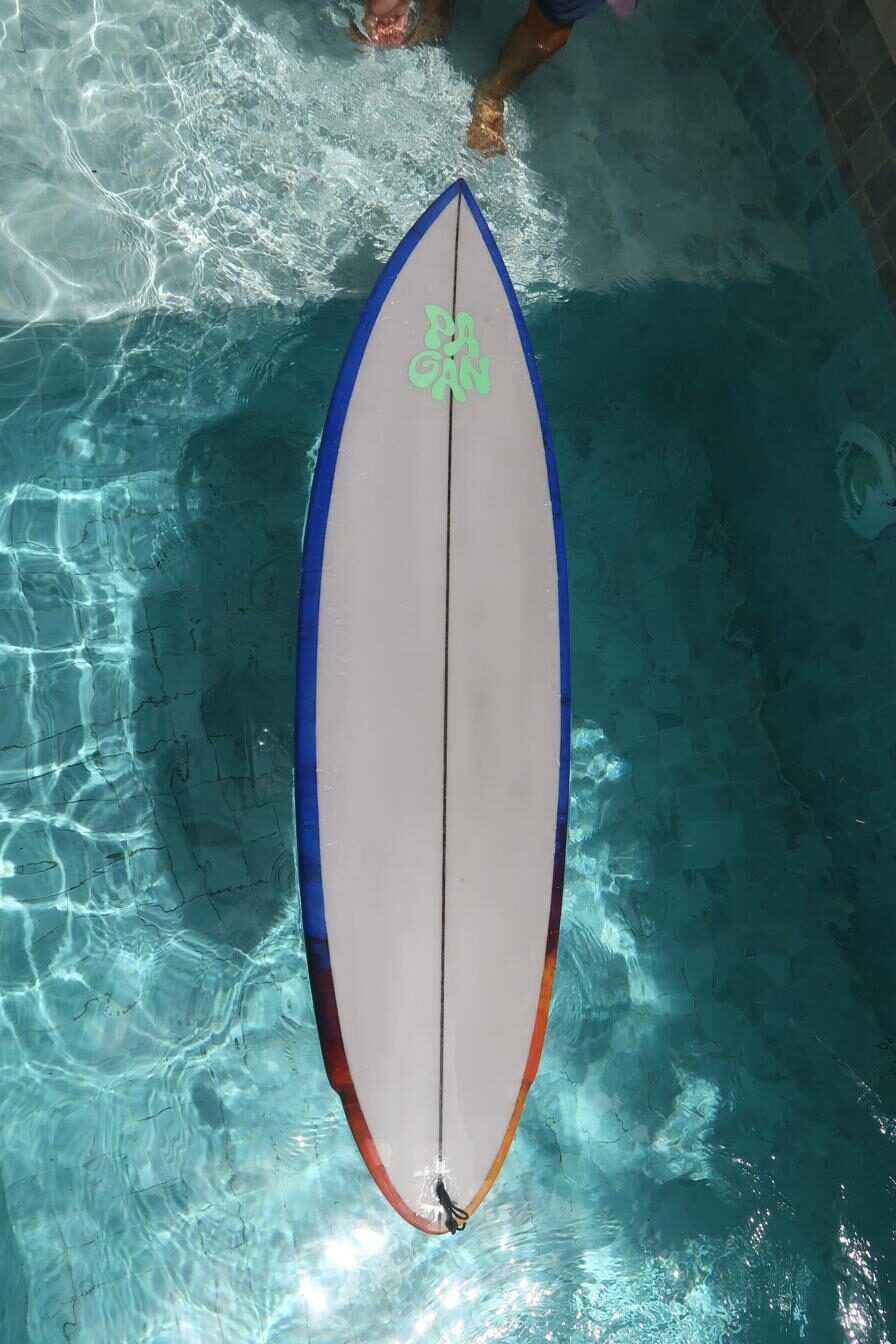 A Pagan surfboard floating in clear water